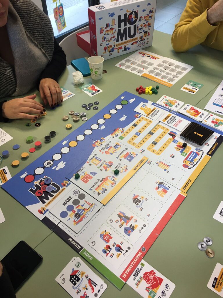 Persone che giocano a Homu Il gioco dell'abitare collaborativo, gioco da tavolo in cui i giocatori collaborano per fare il punteggio più alto